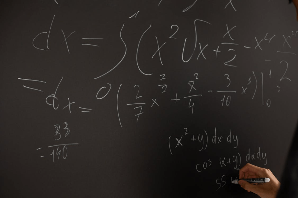 Ecuaciones matemáticas escritas en una pizarra negra con tiza blanca, incluyendo derivadas e integrales.